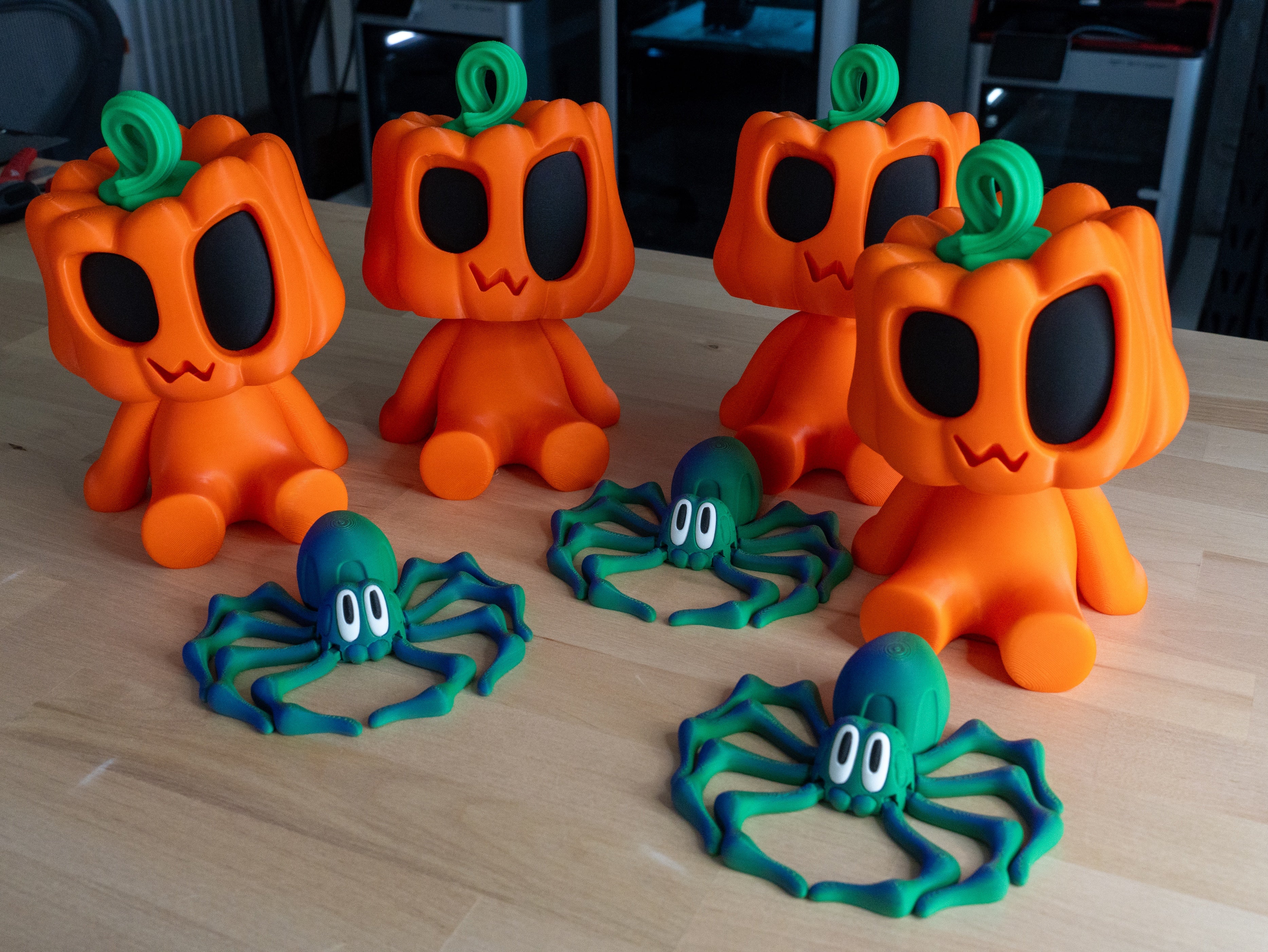 Orange pumpkin-shaped toys with black eyes and green stems, accompanied by green spider toys on a wooden surface.